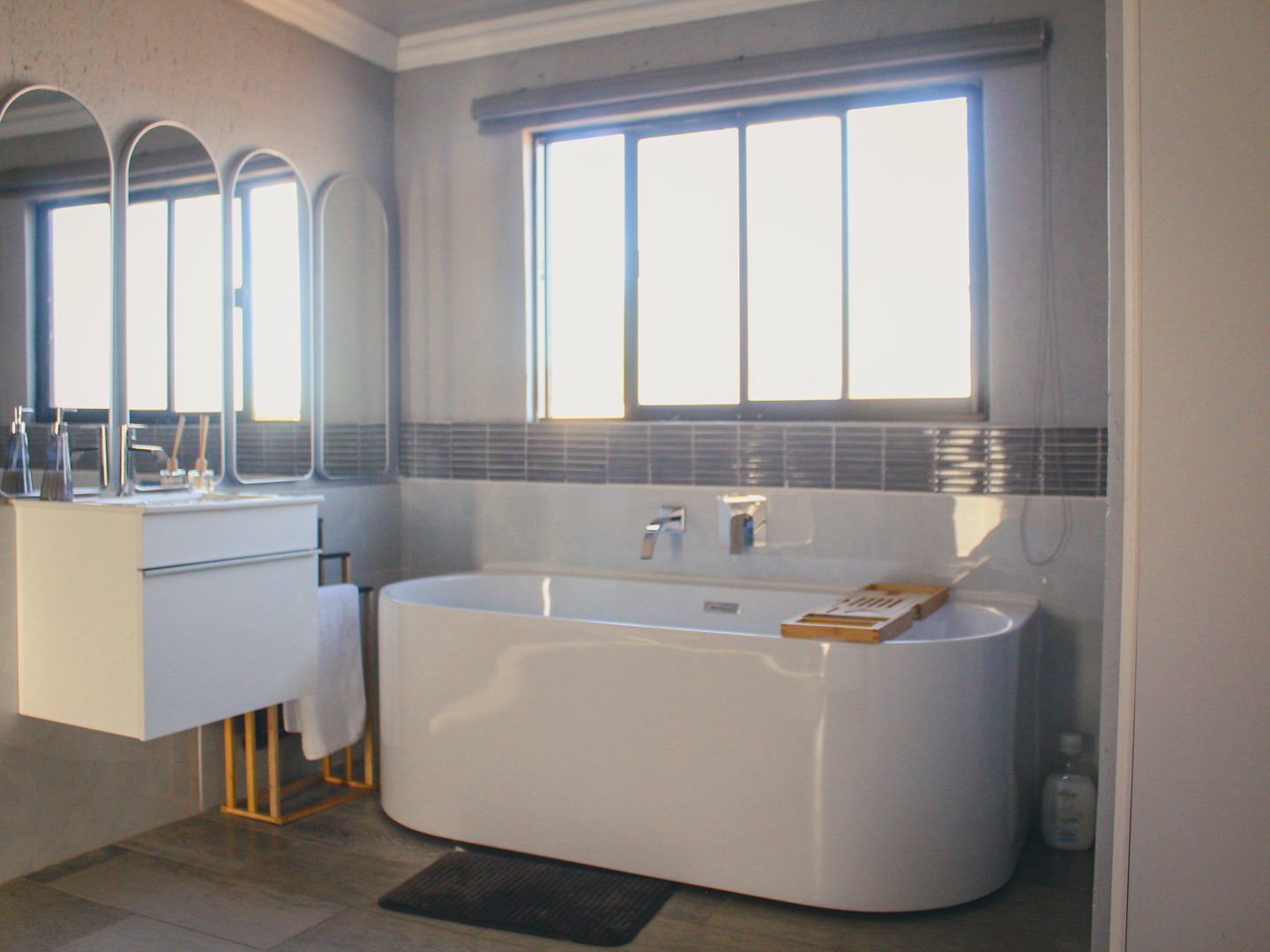 A LAMEMA bathroom with a freestanding oval bath, timber bath caddy and three arched mirrors.