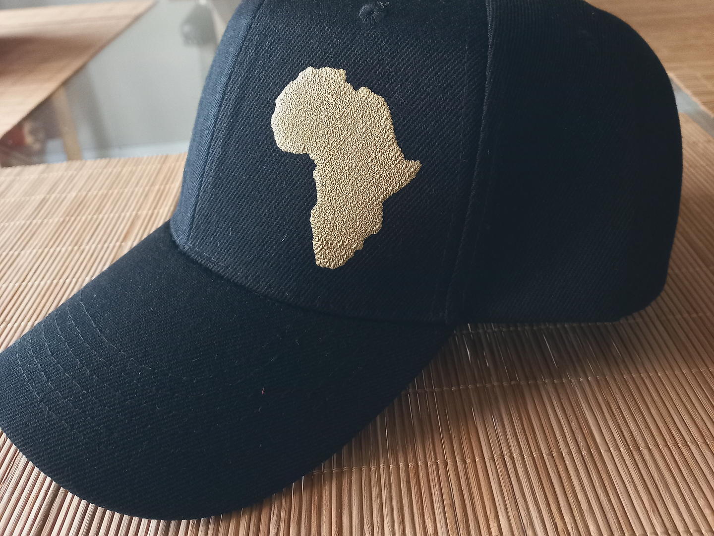 A black cap embroidered with a gold outline of the African continent.