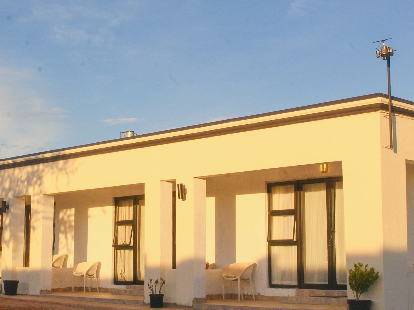 The LAMEMA guest house in Ganyesa at sunset, with a long covered veranda and white chairs outside each room.