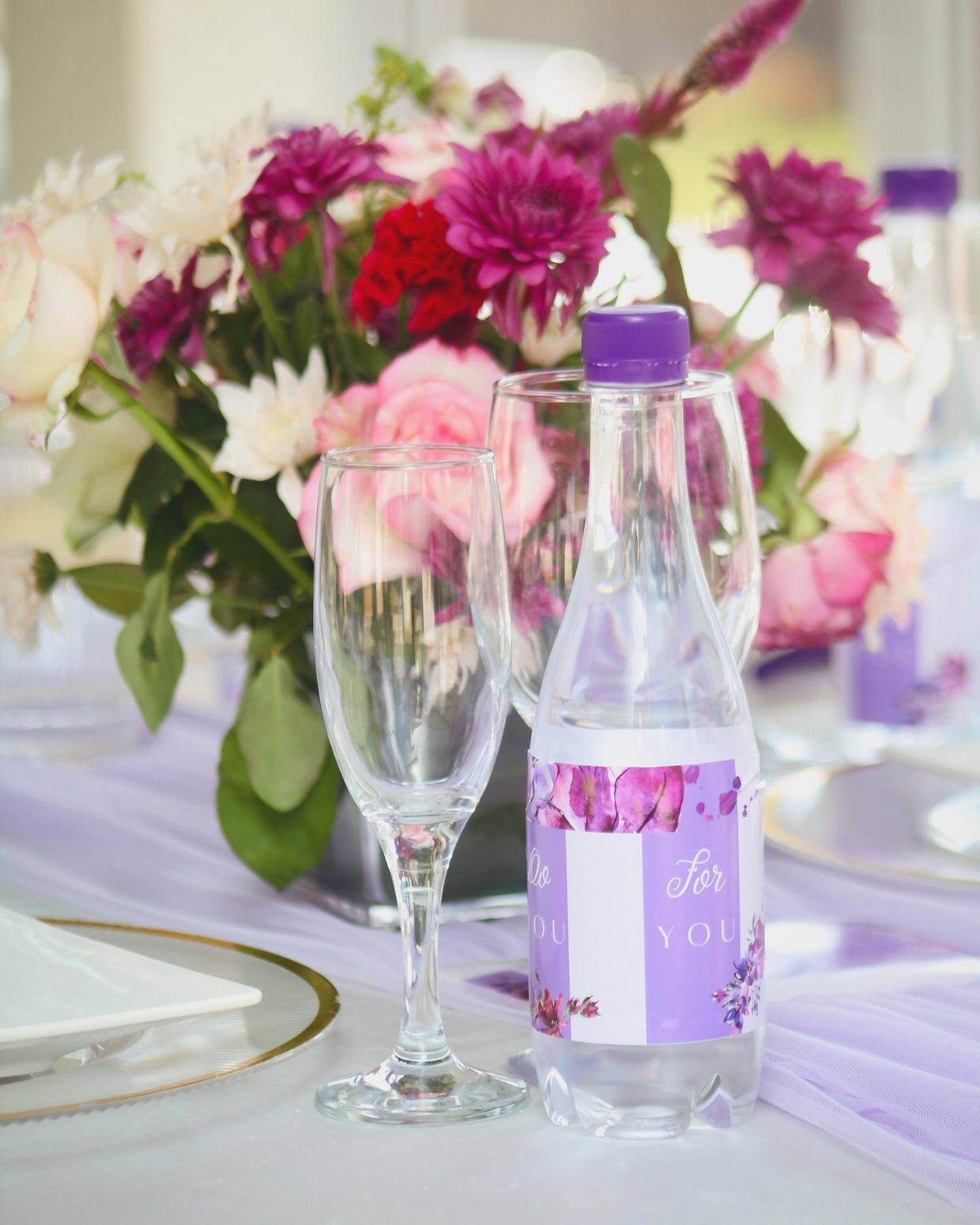 A lilac event table with a pink and burgundy floral centrepiece and a personalised For You water bottle.