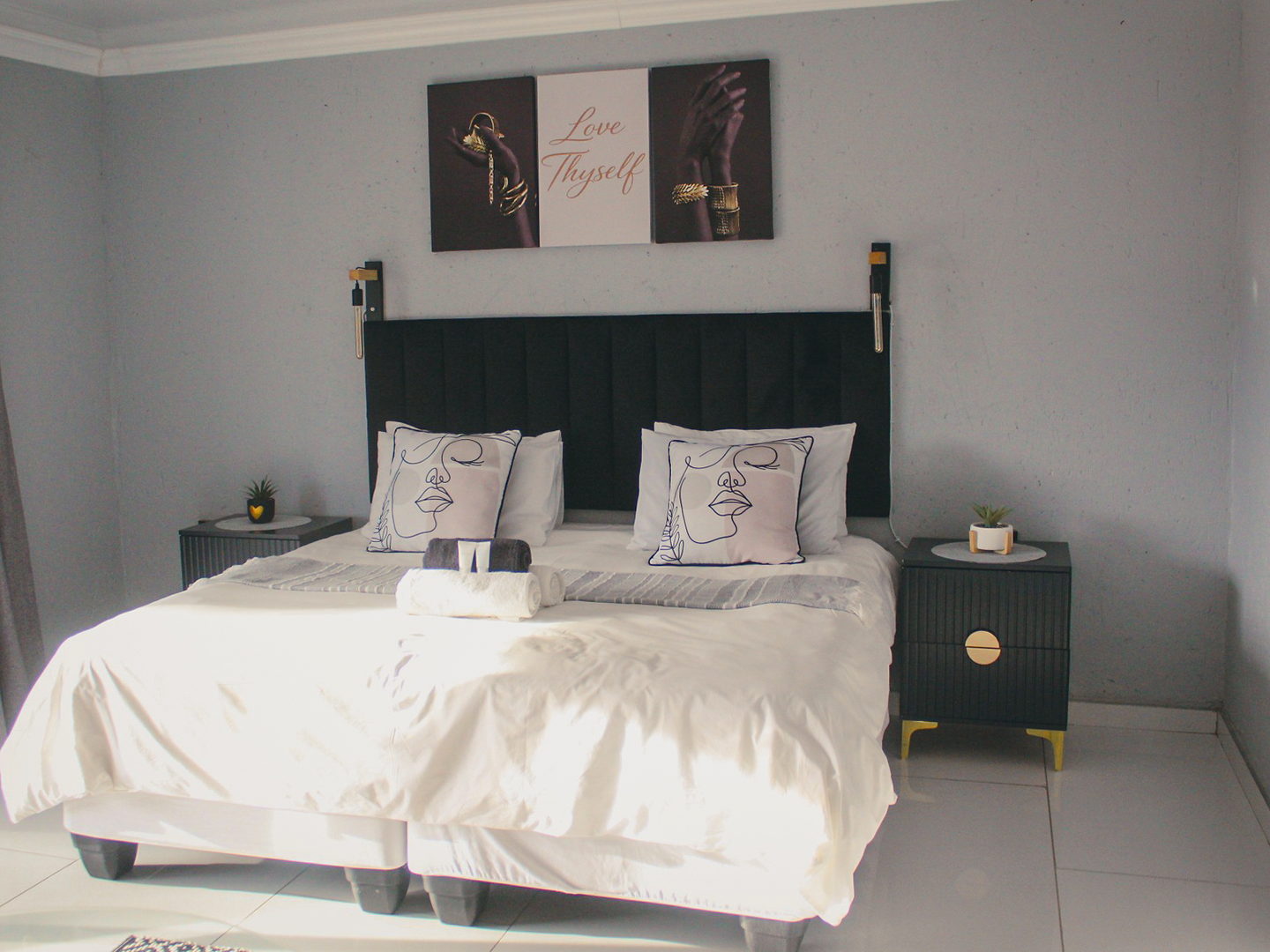 A grey and black LAMEMA guest room with a king bed, line-art scatter cushions and Love Thyself artwork.