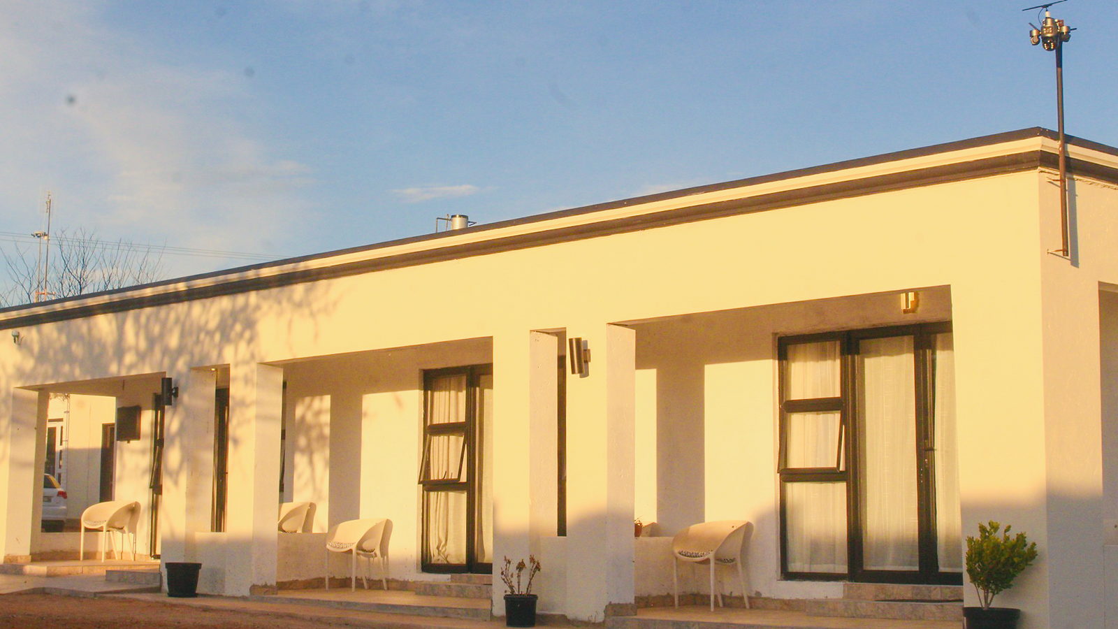 The LAMEMA guest house in Ganyesa at sunset, with a long covered veranda and white chairs outside each room.