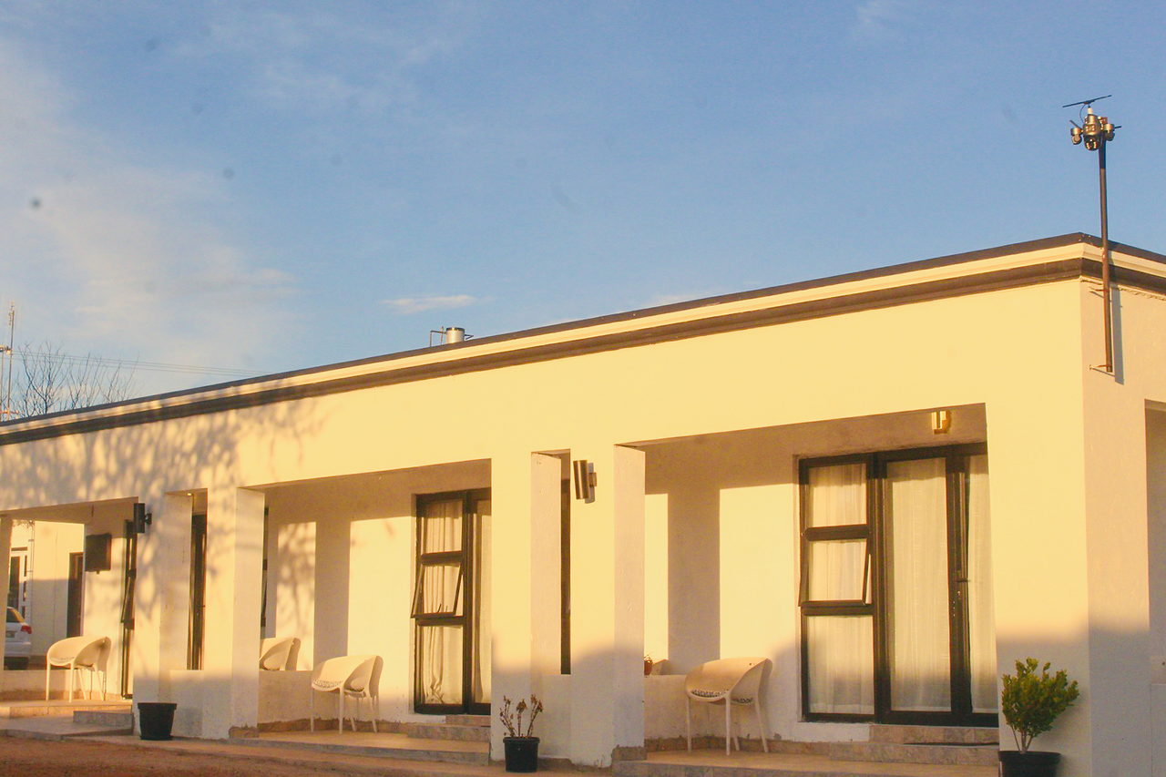The LAMEMA guest house in Ganyesa at sunset, with a long covered veranda and white chairs outside each room.