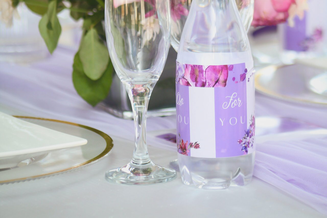 A lilac-styled event table at LAMEMA with a pink and burgundy floral centrepiece and a personalised For You water bottle.