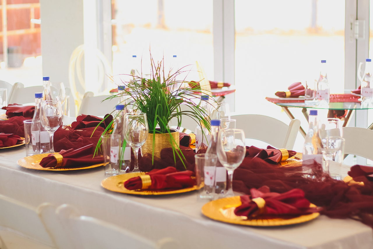 A long table at LAMEMA laid with gold charger plates, burgundy napkins, place cards and a grass centrepiece.