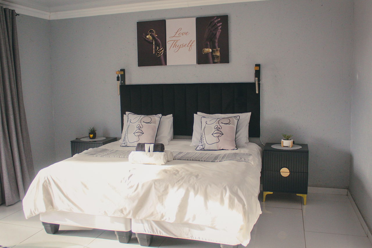A grey and black LAMEMA guest room with a king bed, line-art scatter cushions and Love Thyself artwork on the wall.