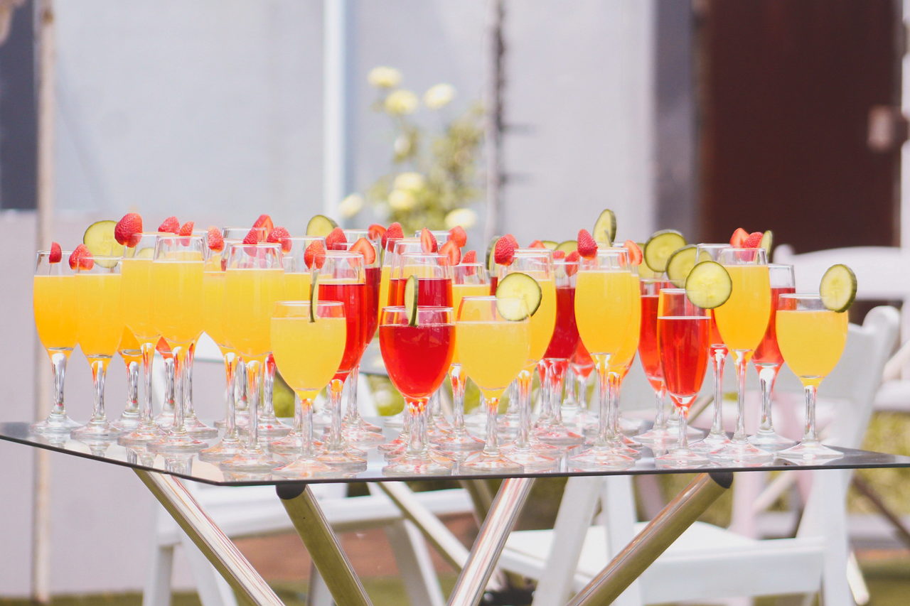A glass table set with rows of orange and red welcome cocktails garnished with strawberries and cucumber at a LAMEMA event.