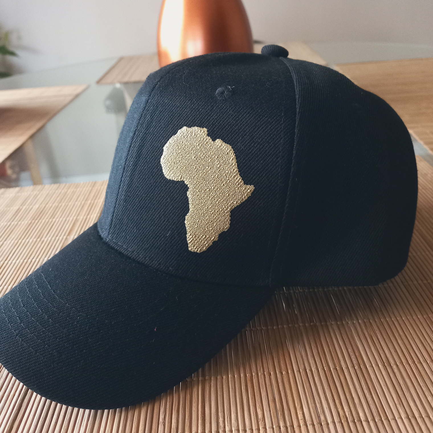 A black cap embroidered with a gold outline of the African continent.