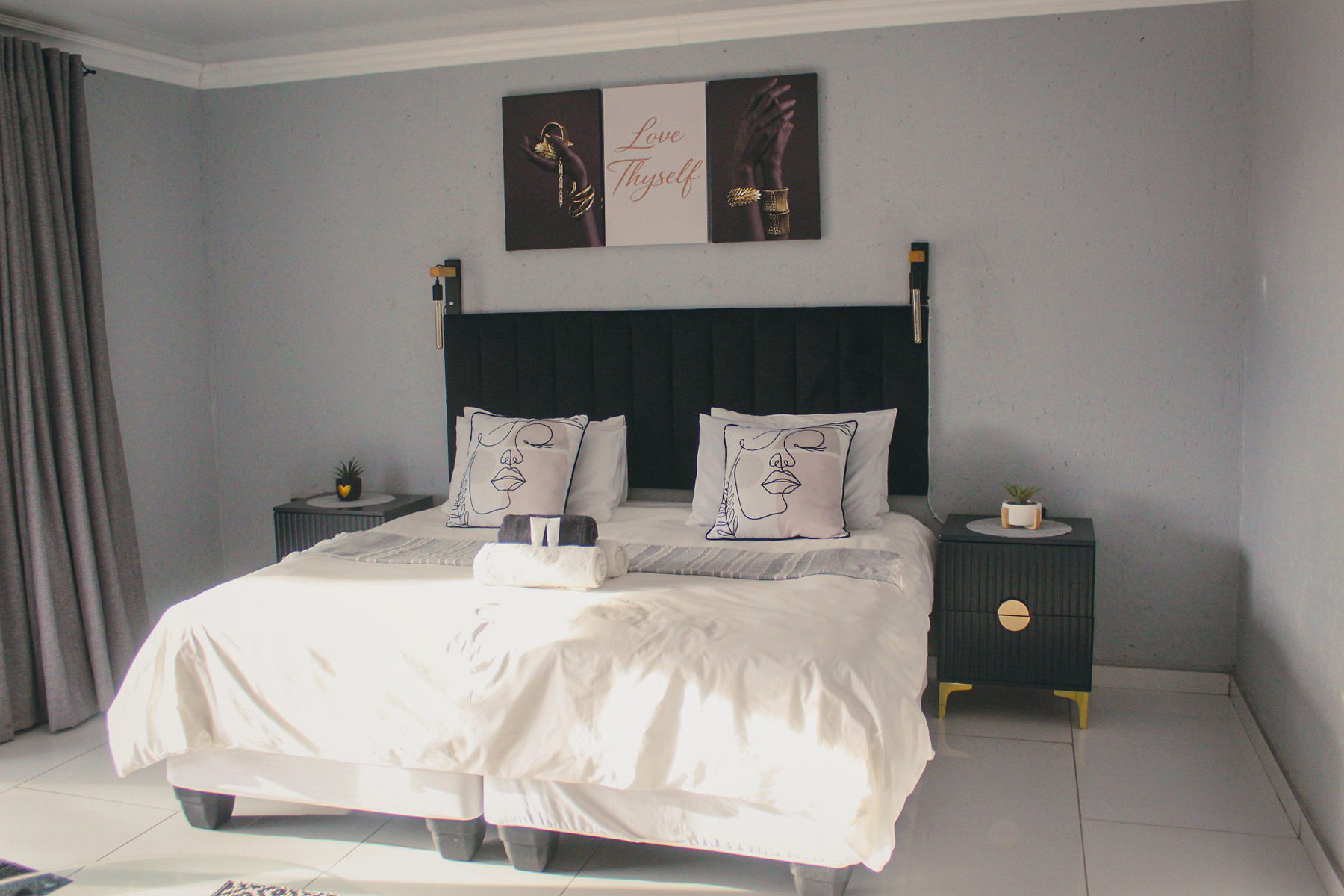 A grey and black LAMEMA guest room with a king bed, line-art scatter cushions and Love Thyself artwork.